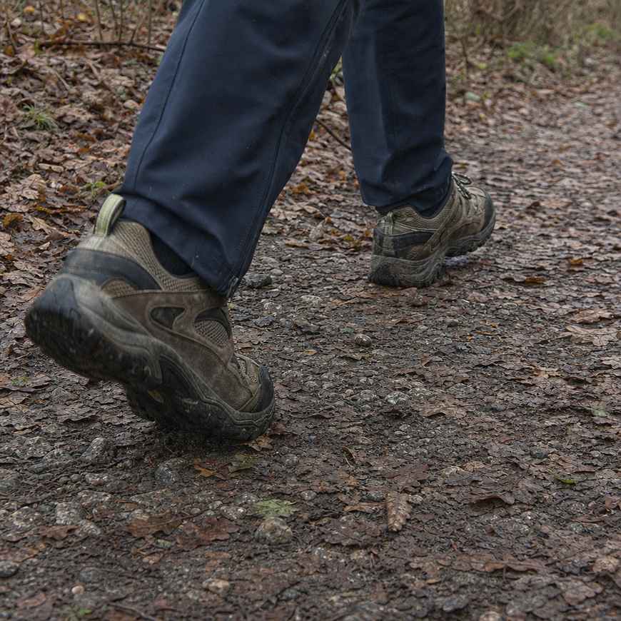 Close-up of worn trail shoes on a leaf-covered path